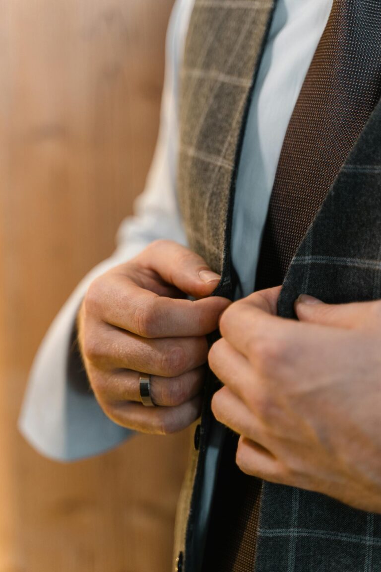 Close-up of a man's hands buttoning a stylish tailored suit, showcasing elegance and craftsmanship.